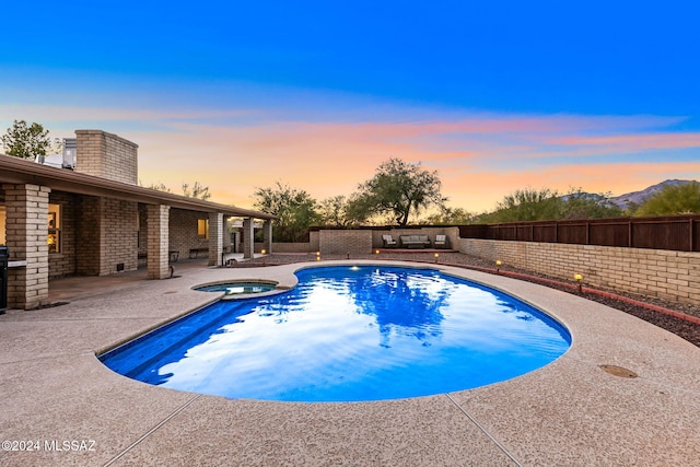 pool at dusk featuring an in ground hot tub and a patio