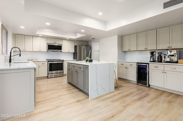 kitchen featuring a center island, stainless steel appliances, a raised ceiling, wine cooler, and gray cabinets