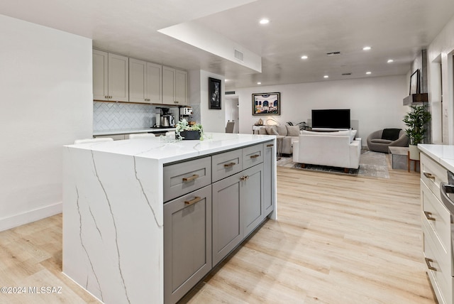 kitchen with gray cabinets, light stone counters, a kitchen island, and light wood-type flooring