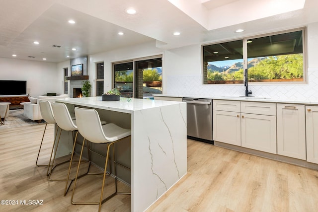 kitchen featuring a center island, white cabinets, sink, stainless steel dishwasher, and light stone countertops