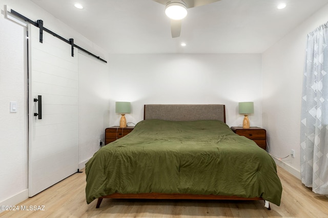 bedroom featuring a barn door, light hardwood / wood-style floors, and ceiling fan