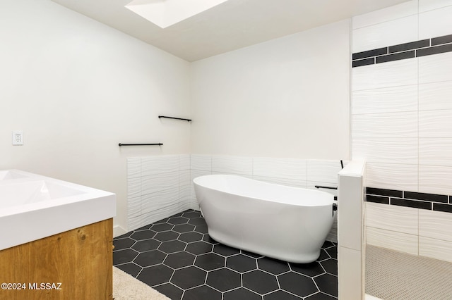 bathroom with a skylight, tile patterned flooring, a tub to relax in, vanity, and tile walls