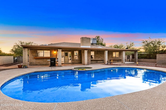 pool at dusk featuring an in ground hot tub and a patio