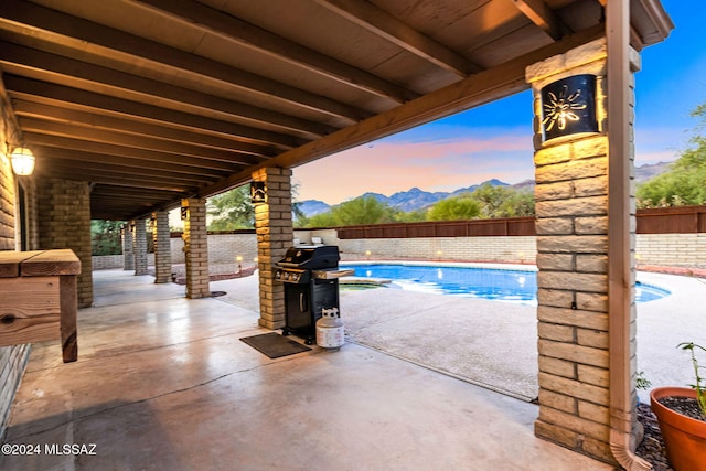 pool at dusk featuring grilling area, a mountain view, and a patio