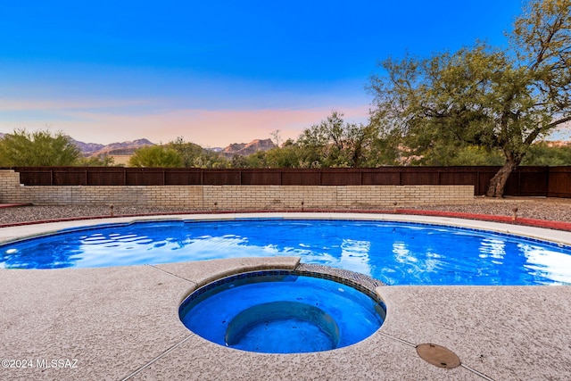 pool at dusk featuring an in ground hot tub and a mountain view