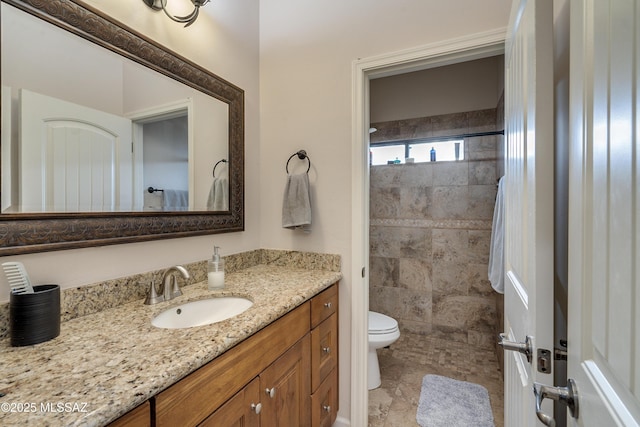 bathroom with toilet, a tile shower, and vanity