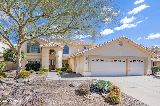 mediterranean / spanish home featuring a tiled roof, stucco siding, an attached garage, and concrete driveway