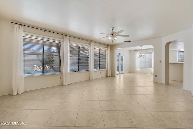 unfurnished room with light tile patterned floors, visible vents, ceiling fan with notable chandelier, and arched walkways