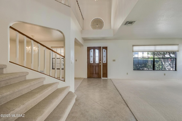 carpeted foyer entrance with visible vents, arched walkways, stairs, tile patterned flooring, and a chandelier