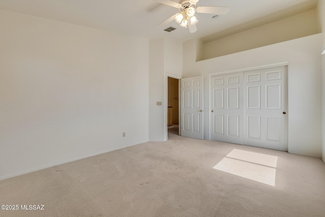 unfurnished bedroom with visible vents, a ceiling fan, a closet, a high ceiling, and carpet flooring