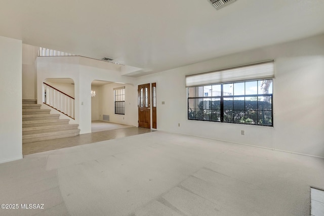 carpeted spare room with visible vents, arched walkways, and stairs