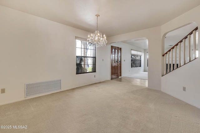 spare room with carpet, visible vents, arched walkways, stairs, and a notable chandelier