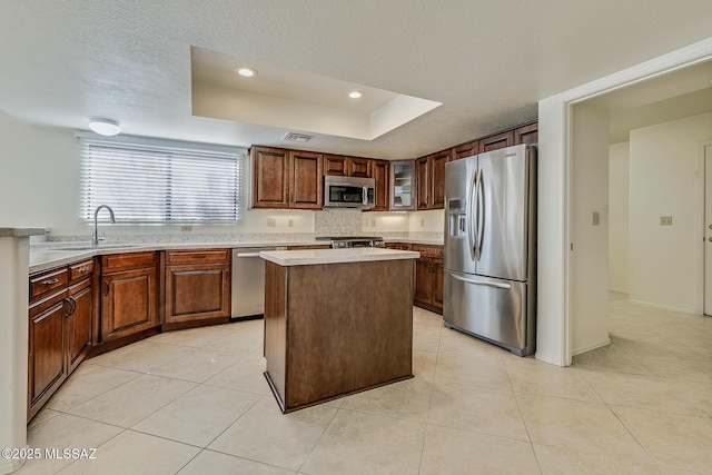 kitchen with a sink, light countertops, appliances with stainless steel finishes, a textured ceiling, and a raised ceiling