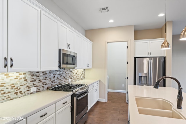 kitchen featuring dark wood-style floors, stainless steel appliances, backsplash, white cabinets, and a sink