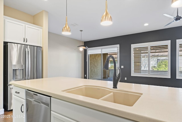 kitchen with decorative light fixtures, stainless steel appliances, light countertops, white cabinets, and a sink