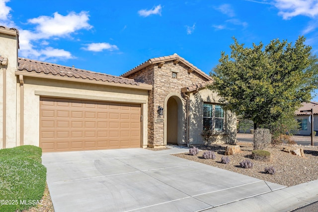 mediterranean / spanish home featuring a garage, concrete driveway, stone siding, a tile roof, and stucco siding