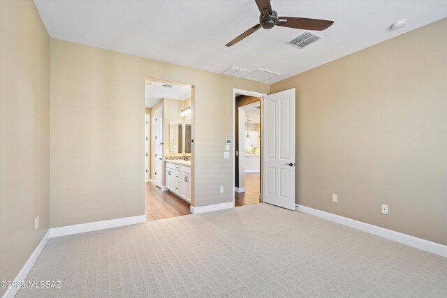 unfurnished bedroom featuring light carpet, a ceiling fan, visible vents, baseboards, and ensuite bath