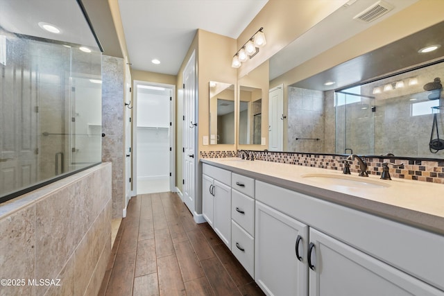 bathroom featuring a shower stall, wood tiled floor, decorative backsplash, and a sink