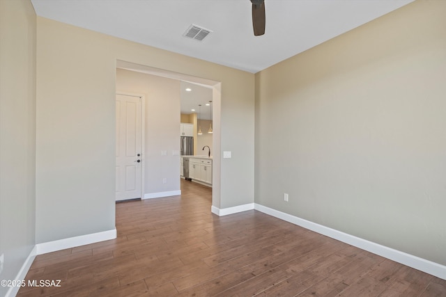 empty room with a sink, baseboards, visible vents, and wood finished floors