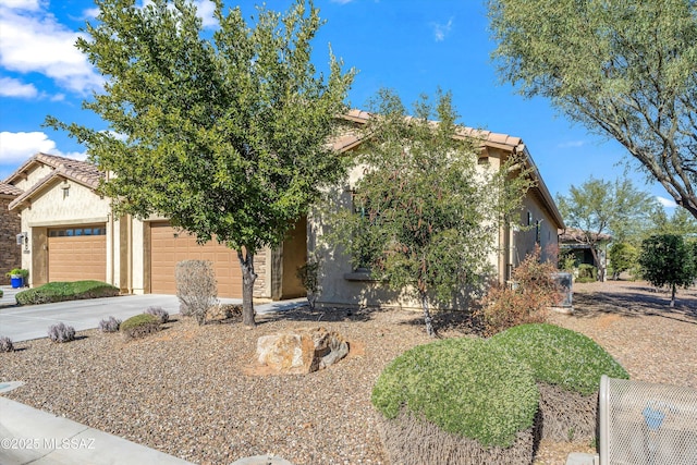 view of property hidden behind natural elements with concrete driveway, an attached garage, and stucco siding