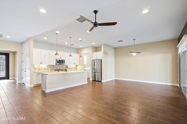 kitchen featuring stainless steel appliances, light countertops, backsplash, open floor plan, and an island with sink