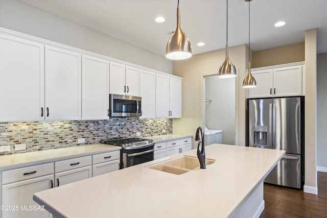 kitchen featuring tasteful backsplash, a center island with sink, washer and clothes dryer, stainless steel appliances, and a sink