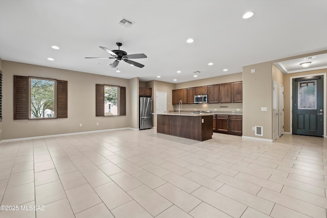 kitchen featuring a kitchen island with sink, light tile patterned floors, stainless steel appliances, and ceiling fan