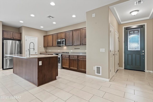 kitchen featuring light tile patterned flooring, appliances with stainless steel finishes, an island with sink, sink, and dark brown cabinetry