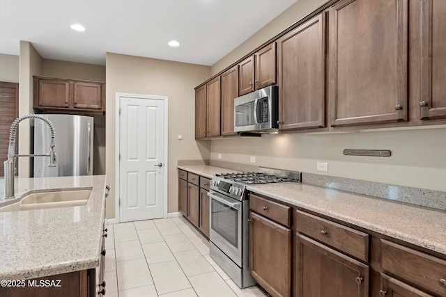 kitchen featuring light tile patterned flooring, sink, light stone counters, dark brown cabinets, and appliances with stainless steel finishes