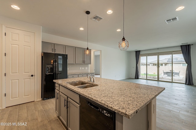 kitchen with black appliances, sink, light stone countertops, an island with sink, and decorative light fixtures