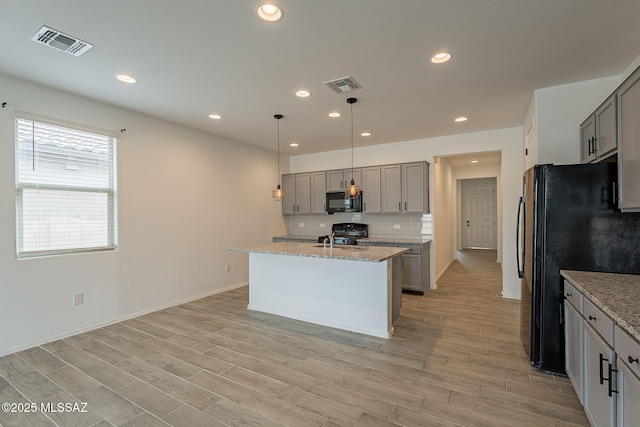 kitchen with pendant lighting, black appliances, a center island with sink, gray cabinets, and light stone counters