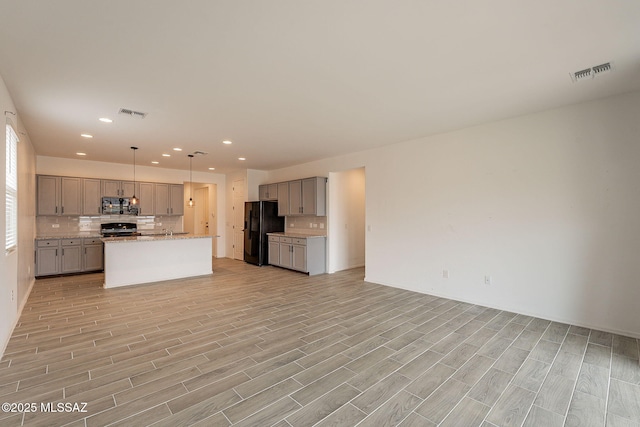 kitchen with pendant lighting, gray cabinetry, black appliances, an island with sink, and light hardwood / wood-style floors