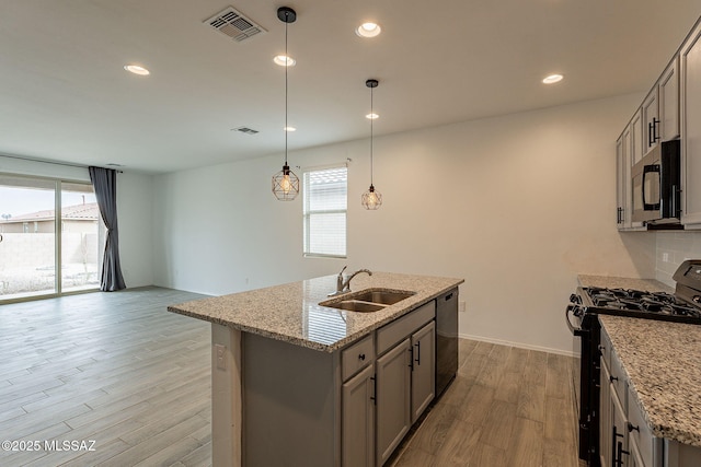 kitchen with light stone countertops, appliances with stainless steel finishes, gray cabinetry, a kitchen island with sink, and hanging light fixtures