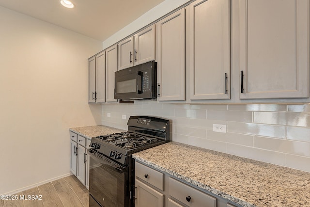 kitchen with light stone countertops, light wood-type flooring, backsplash, gray cabinetry, and black appliances