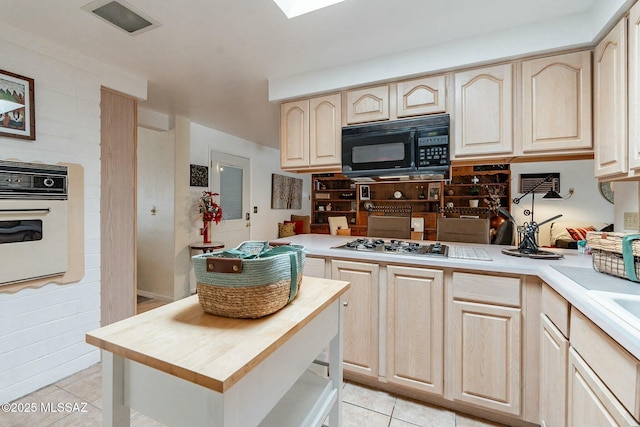 kitchen featuring light tile patterned flooring, stainless steel gas cooktop, light brown cabinetry, and white oven