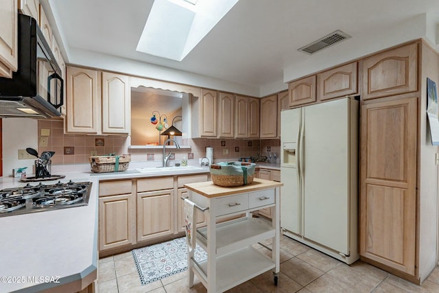 kitchen with light brown cabinets, white fridge with ice dispenser, sink, and a skylight