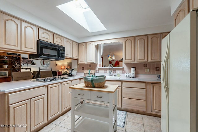 kitchen with a skylight, sink, white fridge with ice dispenser, light brown cabinets, and stainless steel gas stovetop