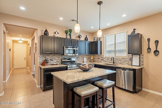 kitchen with appliances with stainless steel finishes, sink, decorative light fixtures, a kitchen island, and light tile patterned flooring