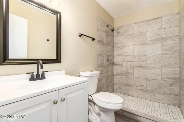 bathroom with a tile shower, vanity, and toilet