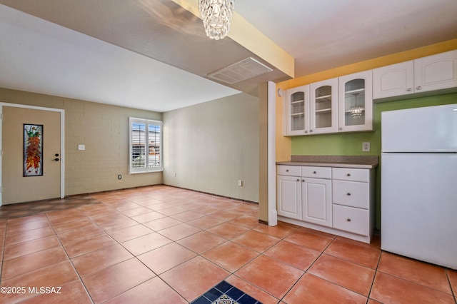 kitchen featuring white fridge, brick wall, light tile patterned floors, a notable chandelier, and white cabinetry