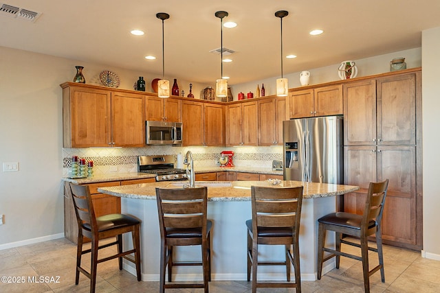 kitchen featuring pendant lighting, a kitchen bar, an island with sink, light stone counters, and stainless steel appliances