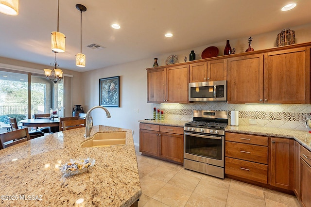 kitchen featuring an inviting chandelier, sink, hanging light fixtures, light stone counters, and stainless steel appliances