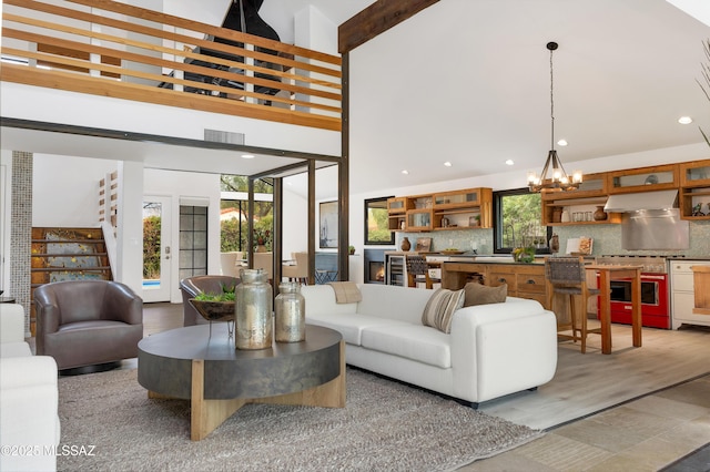 living room with beam ceiling, wood-type flooring, a high ceiling, and an inviting chandelier