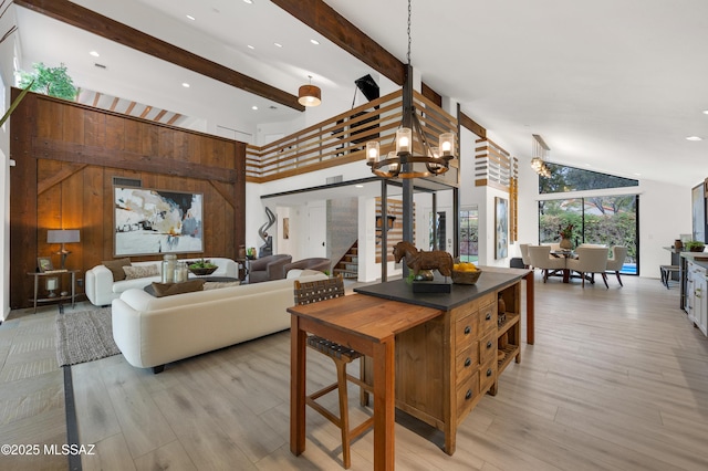 living room featuring light wood-type flooring, high vaulted ceiling, an inviting chandelier, and wood walls