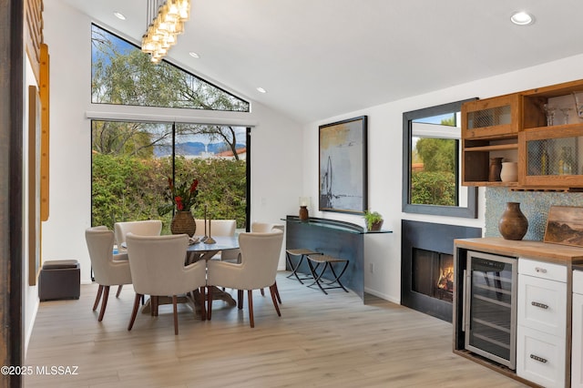 dining area with wine cooler, light hardwood / wood-style floors, and vaulted ceiling