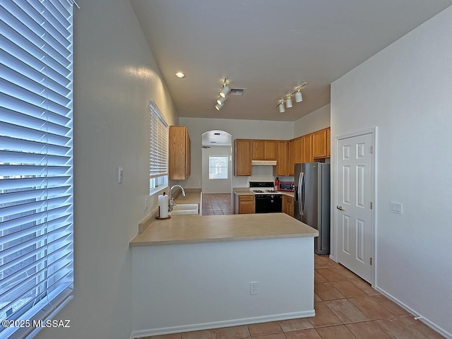 kitchen featuring light tile patterned flooring, gas stove, sink, stainless steel fridge, and kitchen peninsula