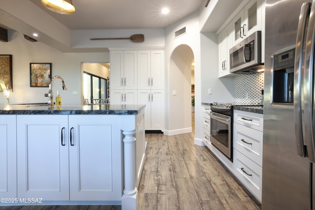 kitchen featuring white cabinets, appliances with stainless steel finishes, backsplash, and light wood-type flooring