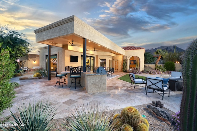 patio terrace at dusk with an outdoor living space, ceiling fan, a mountain view, and an outdoor bar