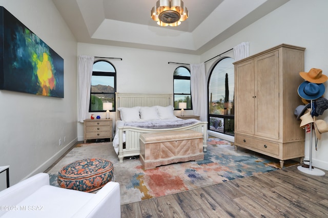 bedroom with a tray ceiling, dark hardwood / wood-style floors, and an inviting chandelier