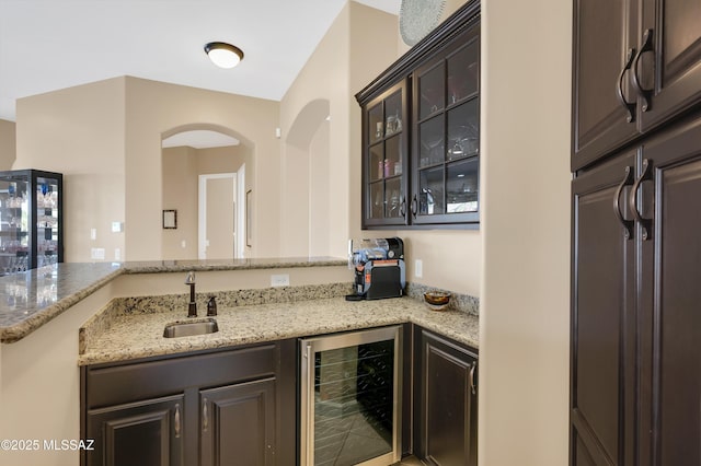 kitchen with dark brown cabinets, light stone counters, wine cooler, and sink